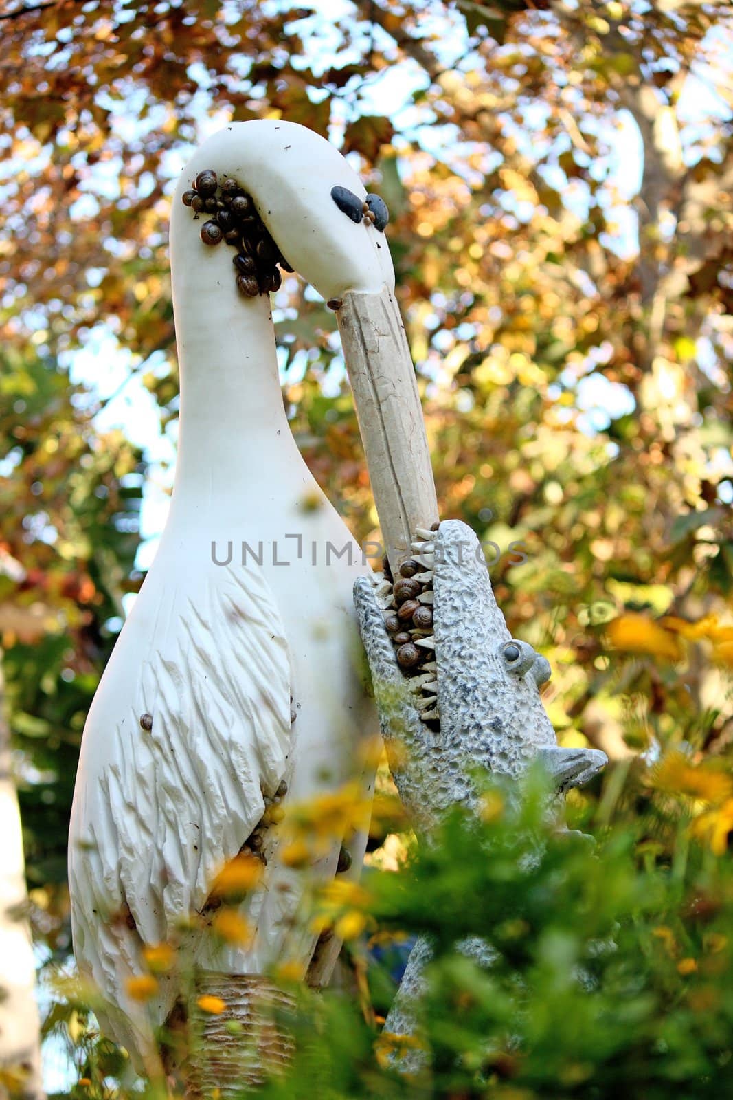 Crazy statue of a stork feeding a croc, on a autumn leaf surrounding setting, with snails on a garden of Faro, Portugal.