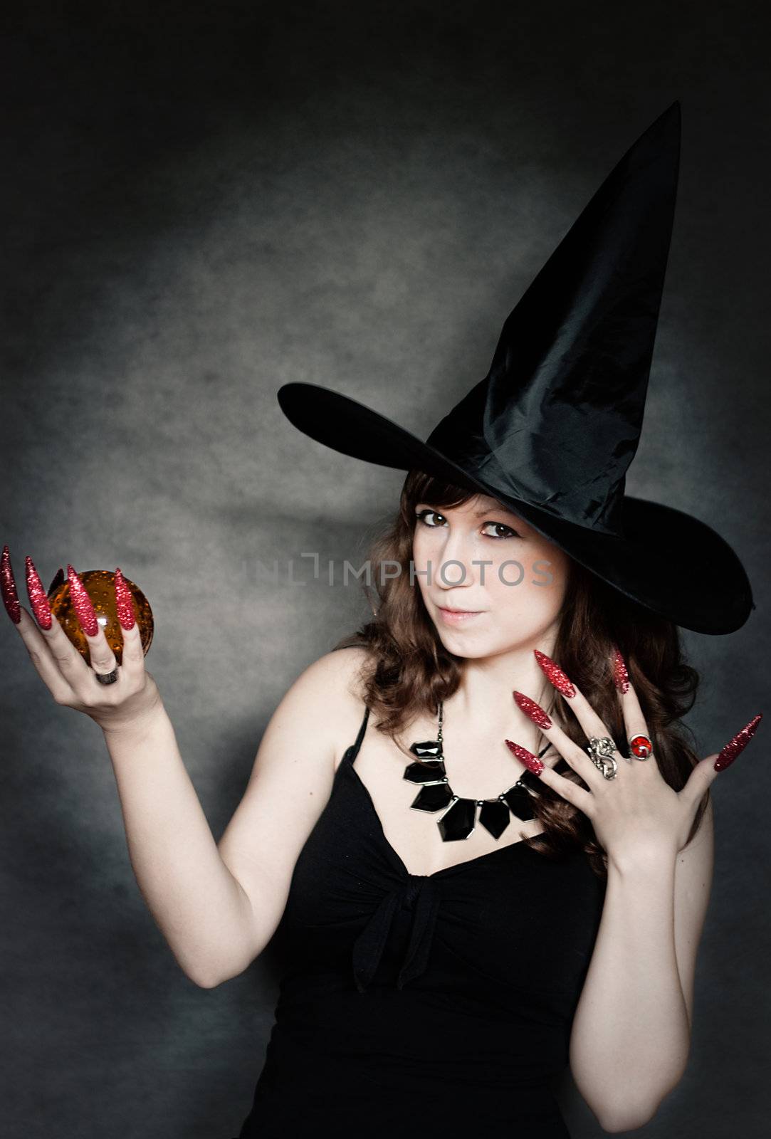 Pretty young witch with black hat, long nails and crystal ball