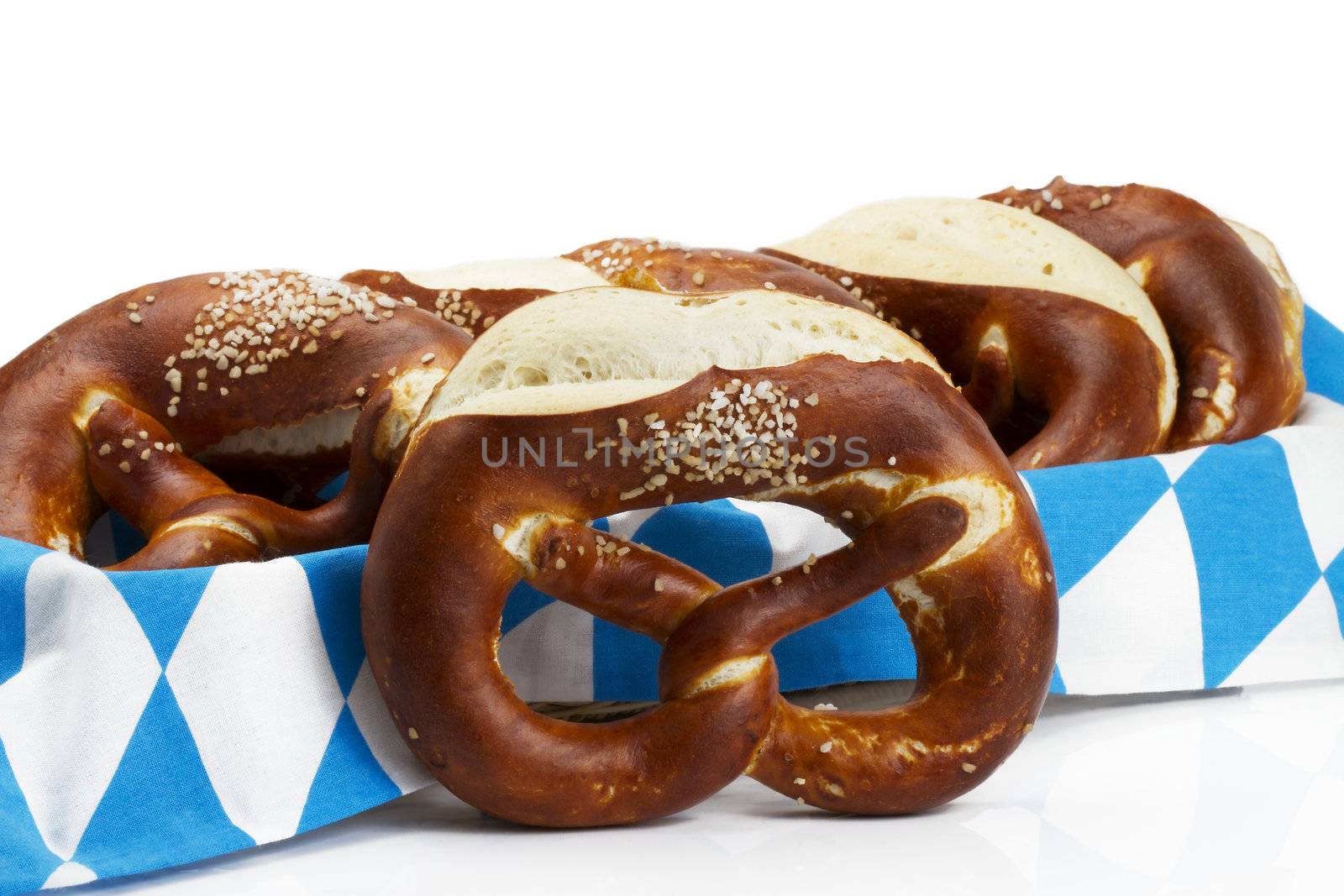 pretzel in front of pretzels in a bread basket with bavarian towel on white background