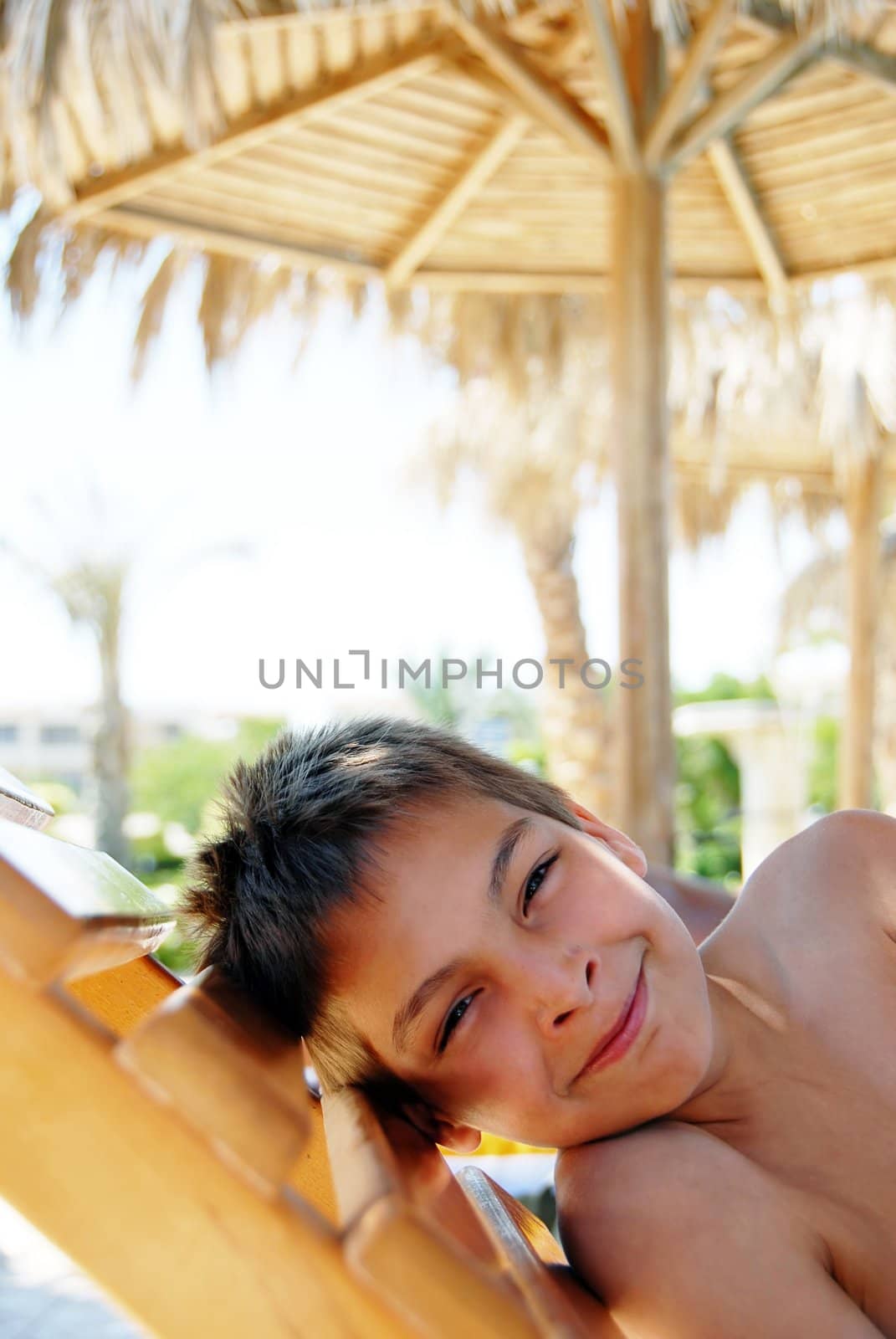 smiling teenage boy portrait lying under sunshade on beach
