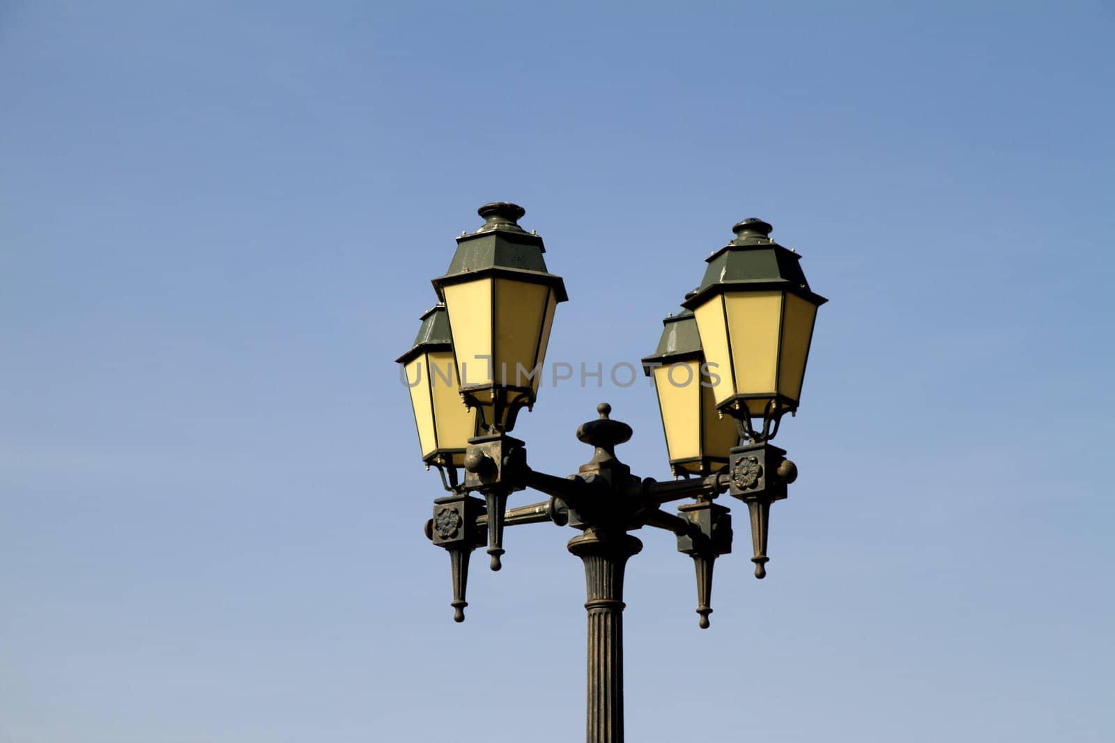 Close view of a four headed street light over a blue sky.