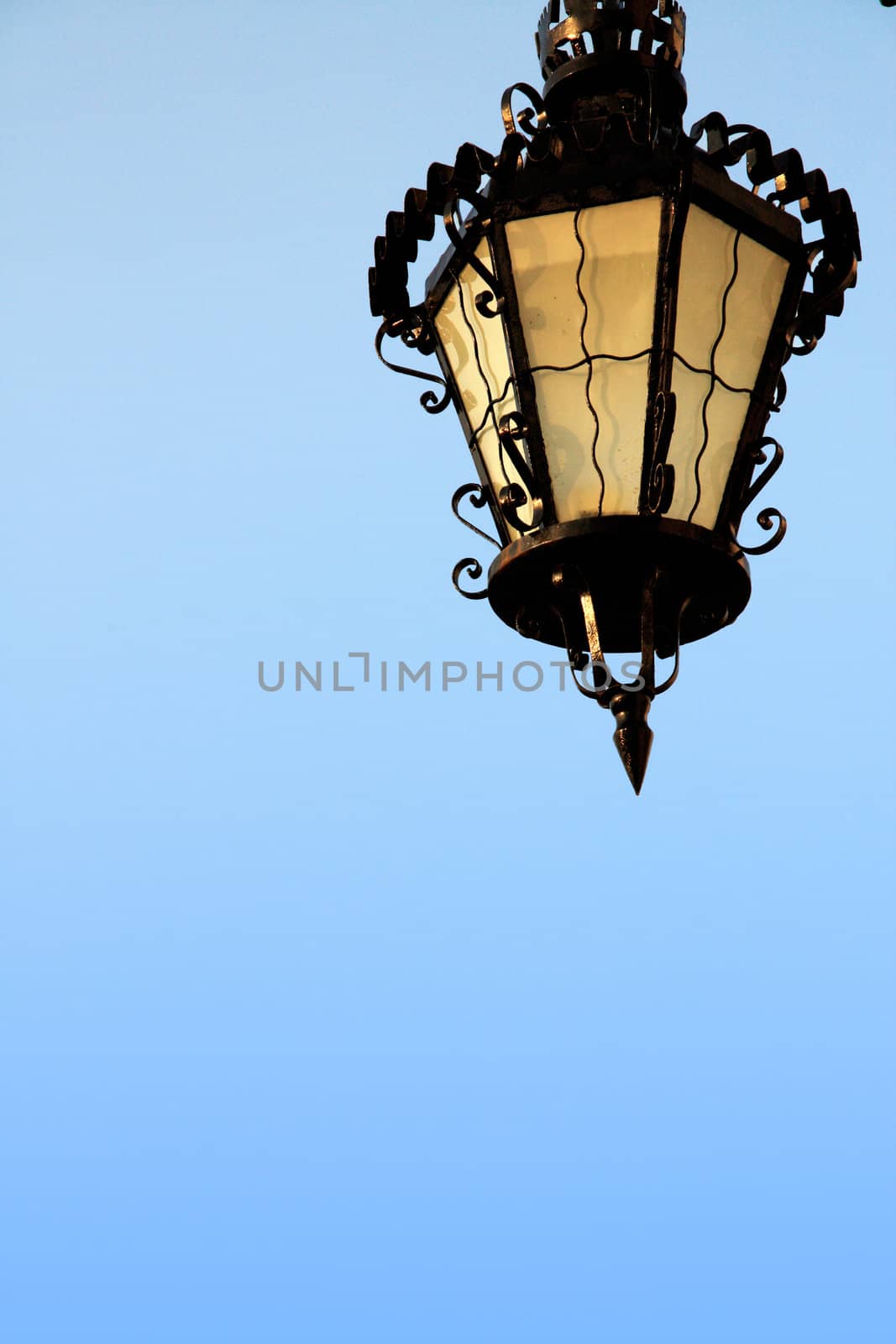 Close up view of a vintage street lamp over a blue sky.