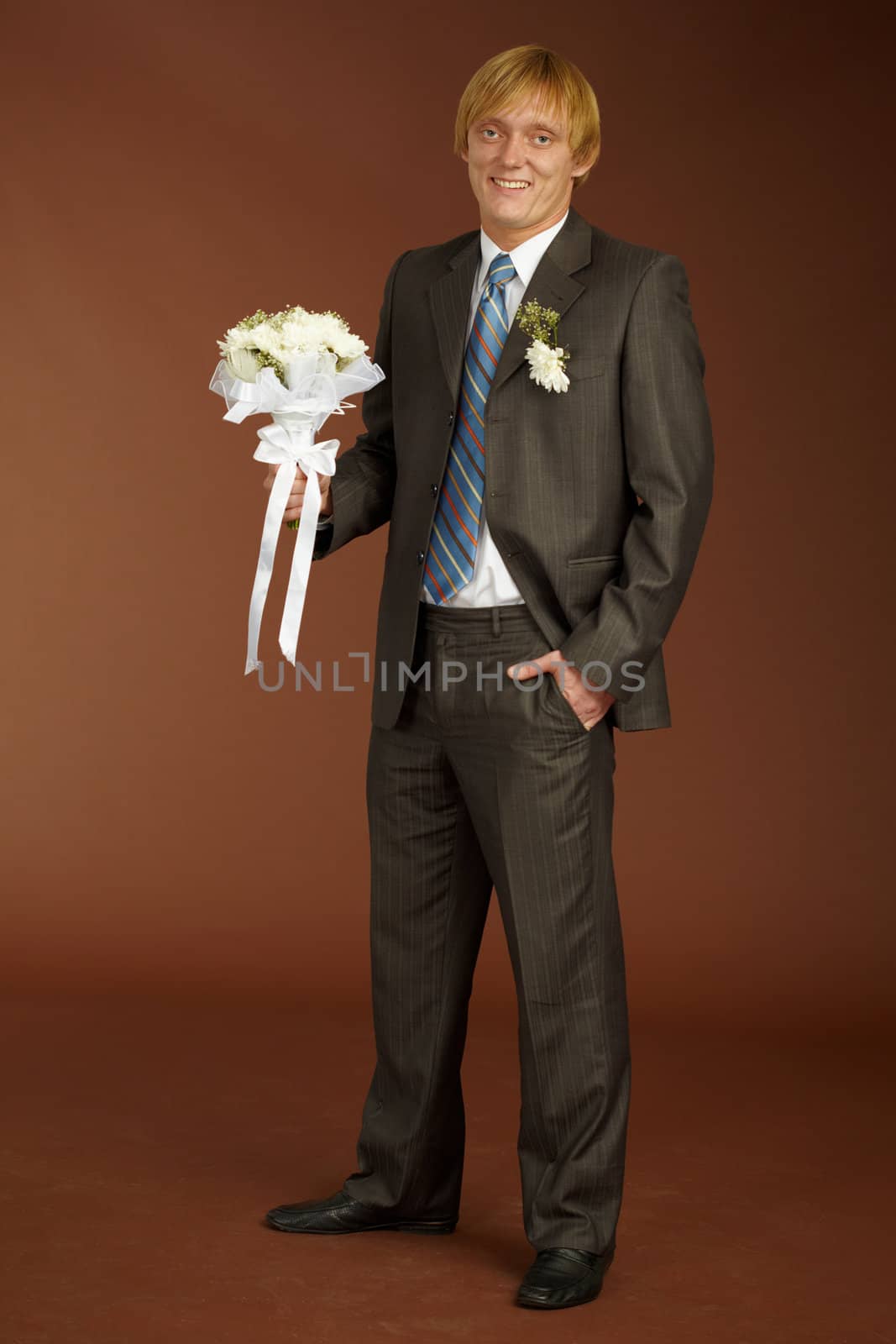 Happy groom with a bouquet on brown background