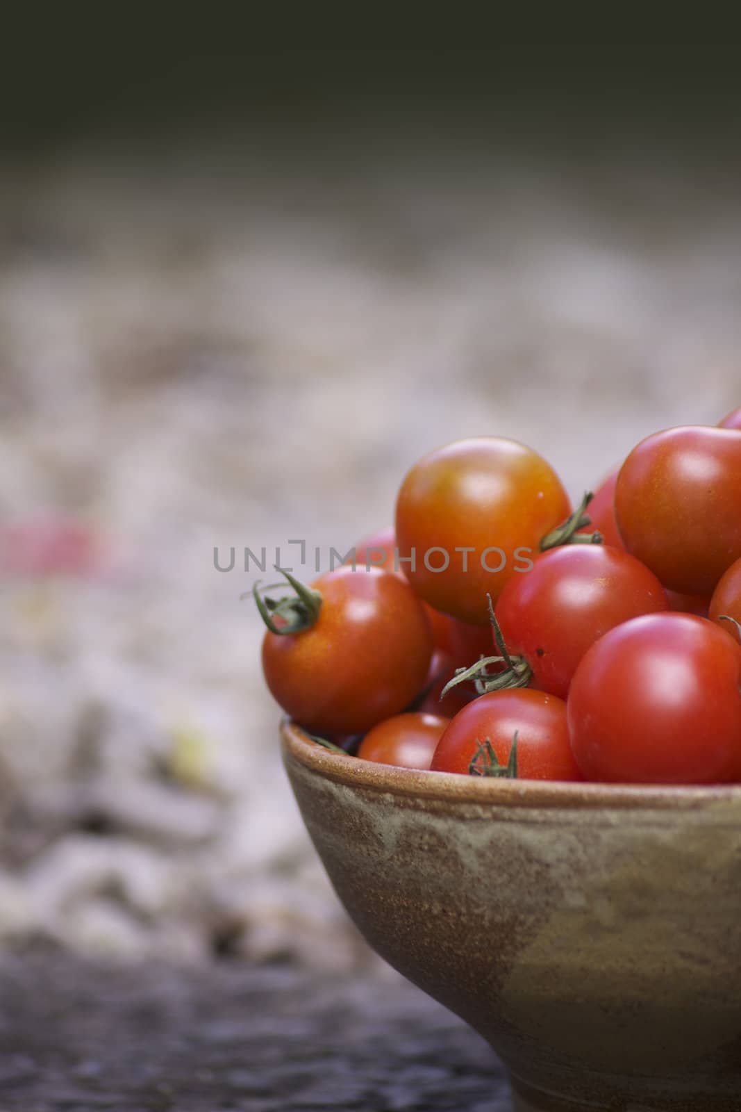 Close up detail of a freshly picked organically grown small red tomatoes, in a brown ceramic bowl. Set on a portrait format with room for copy etc above.