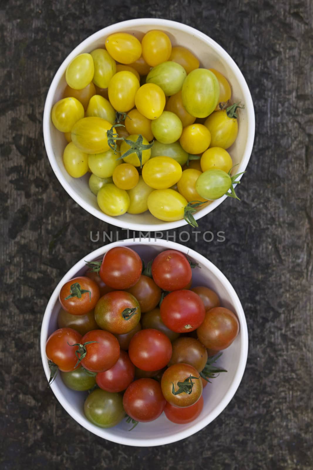 Two bowls of freshly picked organically grown tomatoes. Image taken from above. One bowl contains small red tomatoes, the other small yellow pear shaped tomatoes.