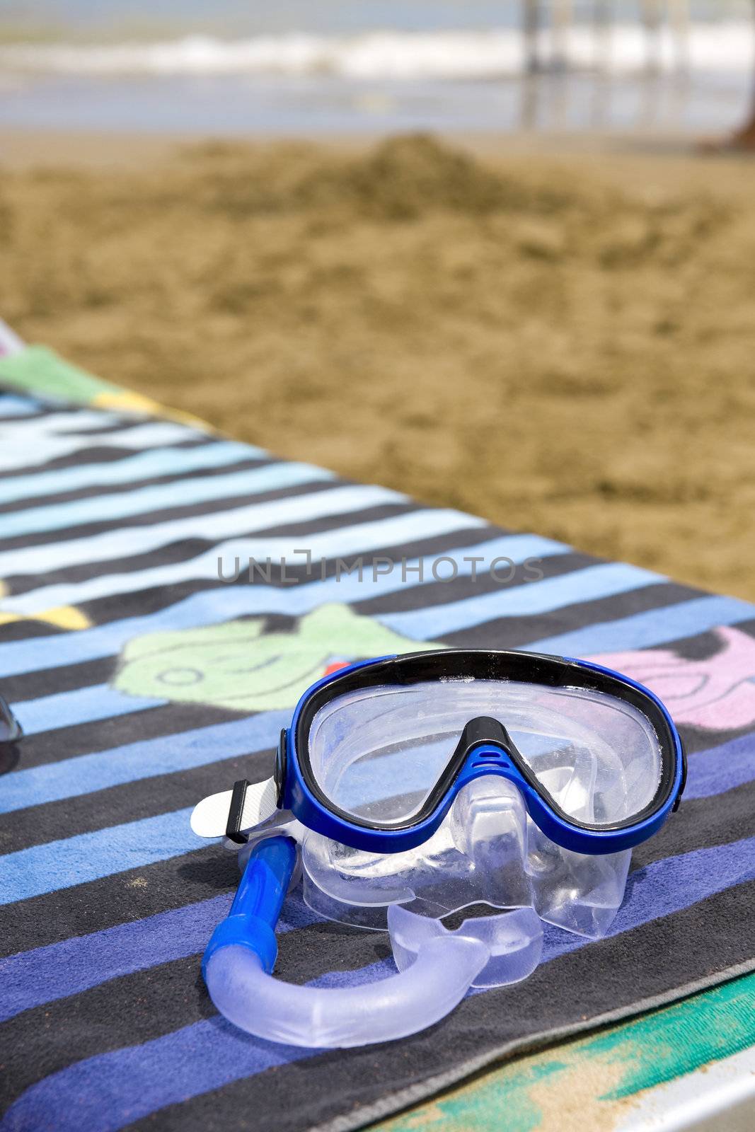 a mask on a  towel and a beach chair, near the water of the ocean