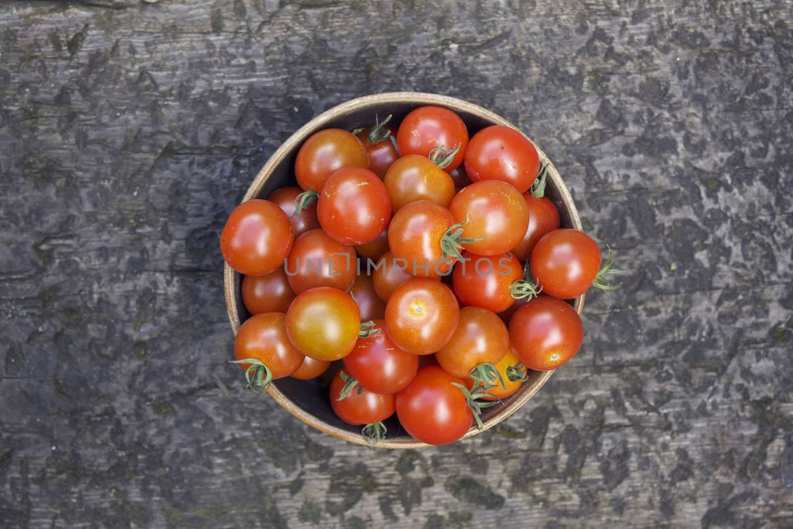 A single bowl of small round shaped red tomatoes in a brown ceramic bowl shot from above.