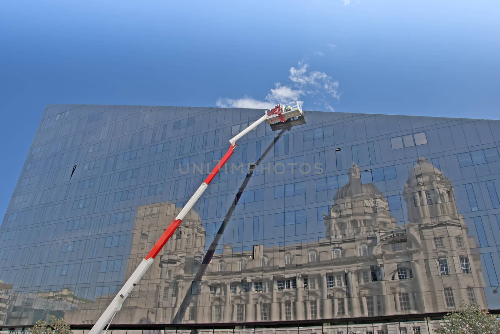 A Red and White Cherry Picker and Glass Building with Reflection of Historic Building