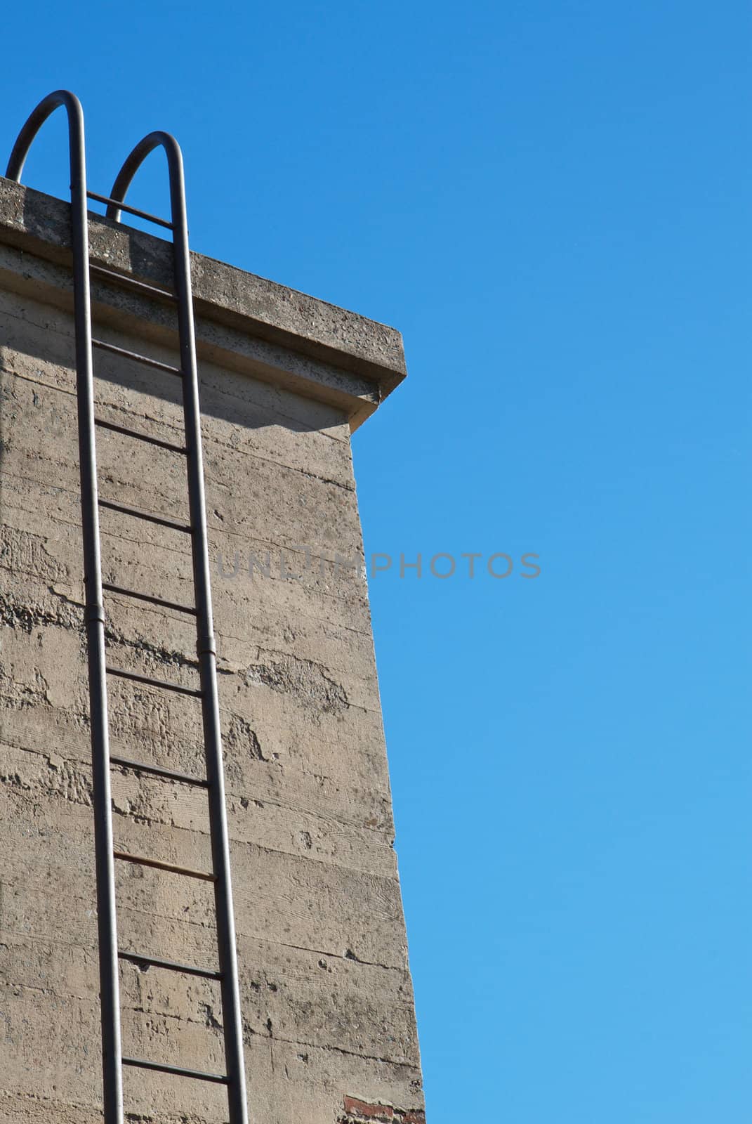 Steel ladder up concrete wall with blue sky background