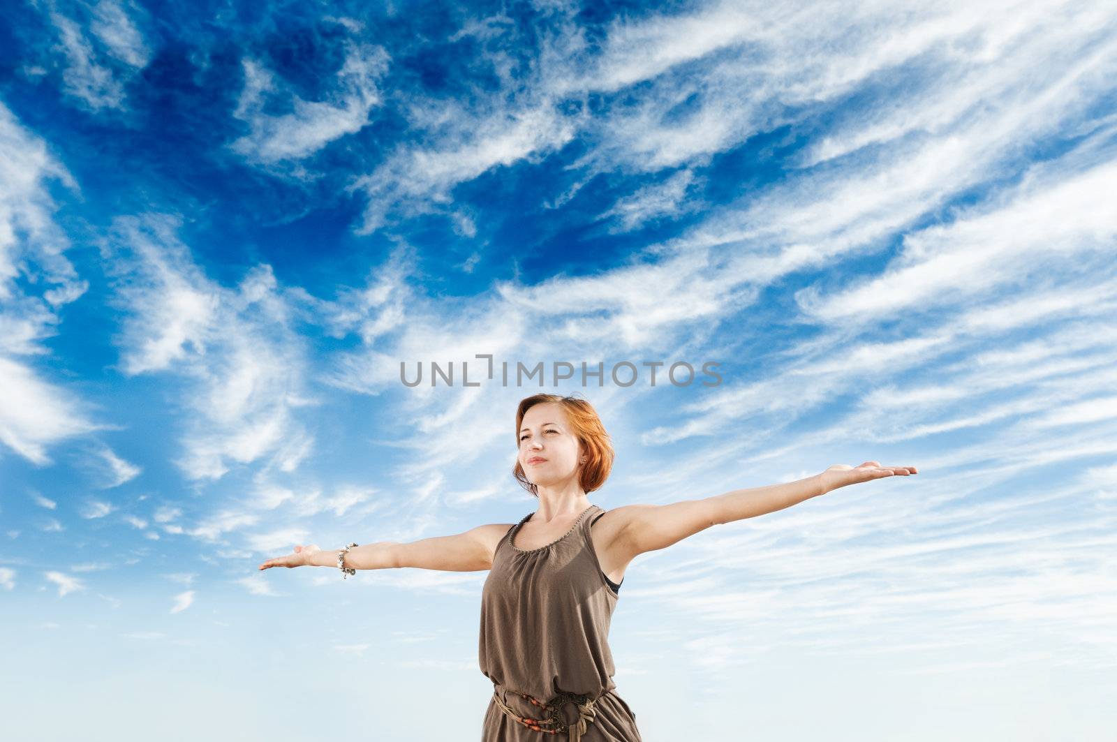 Beautiful young dancer performing yoga-dance outdoors with blue sky and clouds in the background