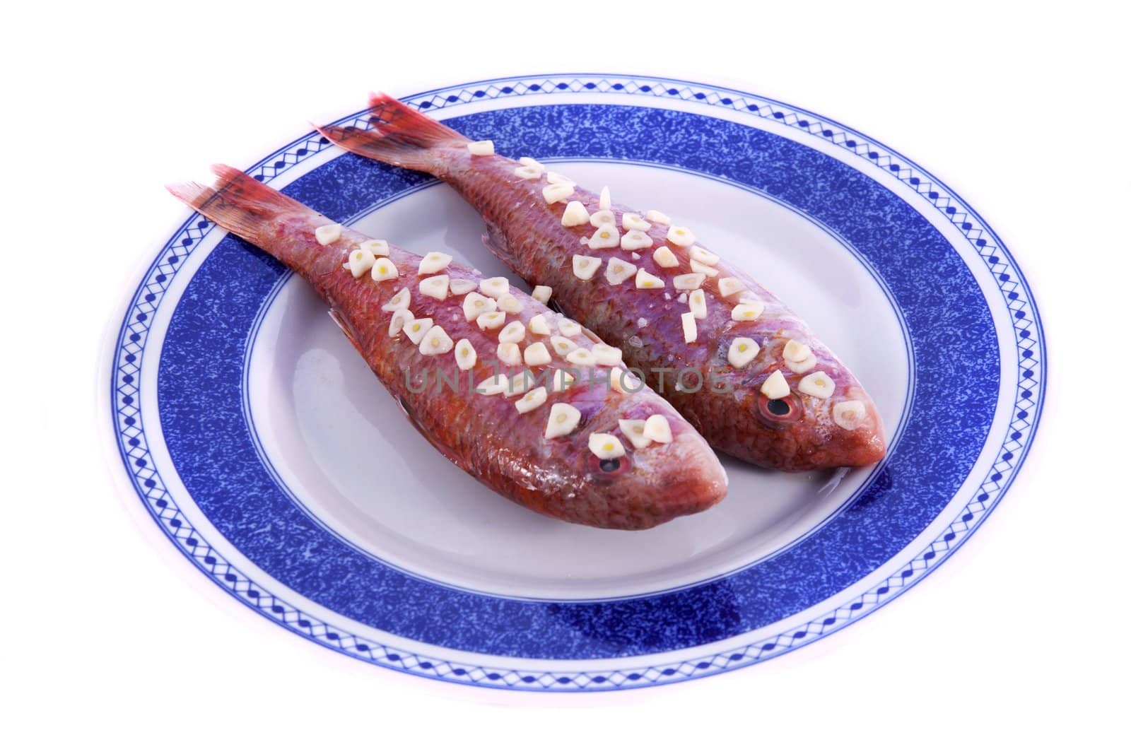 Detail view of two red fish on a plate with garlic on top ready to be made.