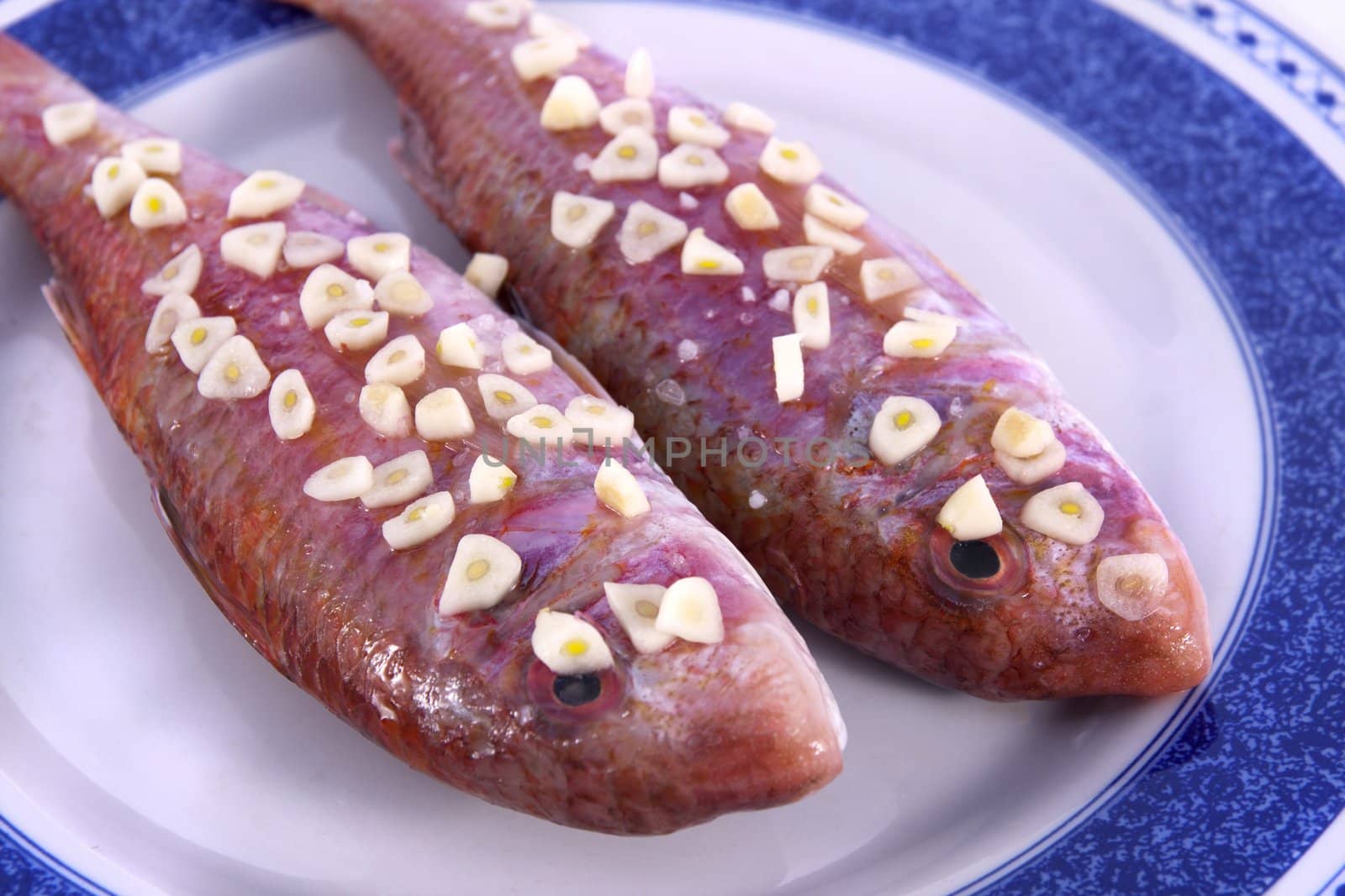 Detail view of two red fish on a plate with garlic on top ready to be made.