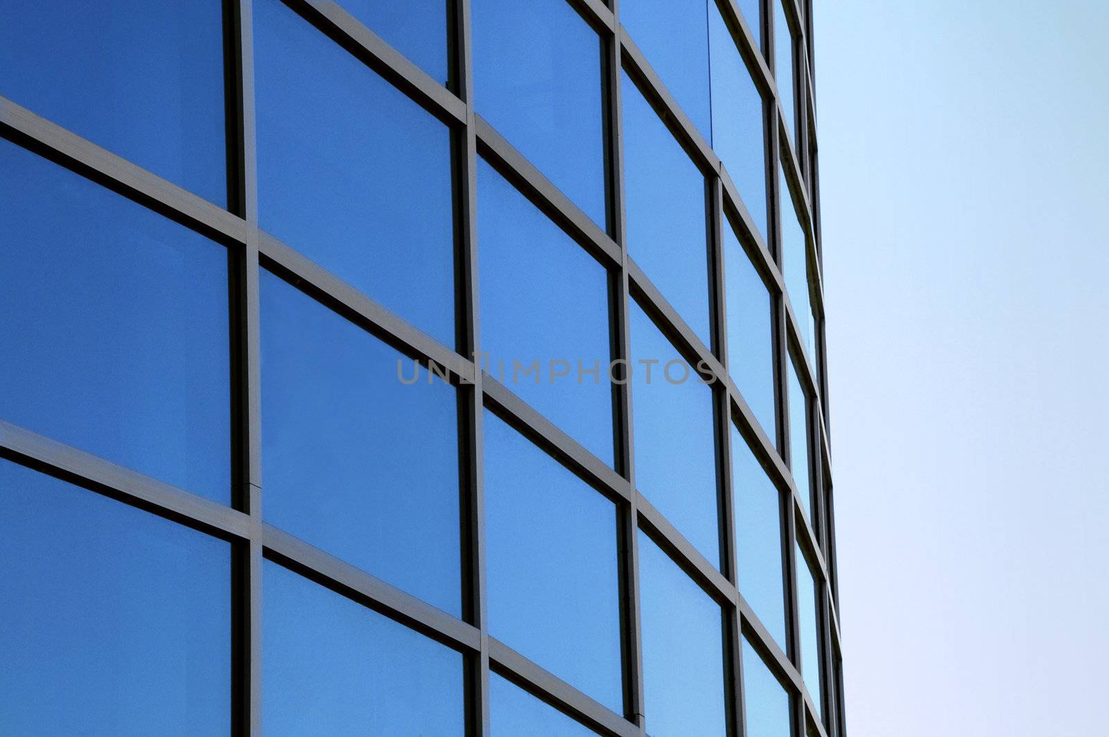 Curved exterior windows of a commercial office building reflecting a blue sky