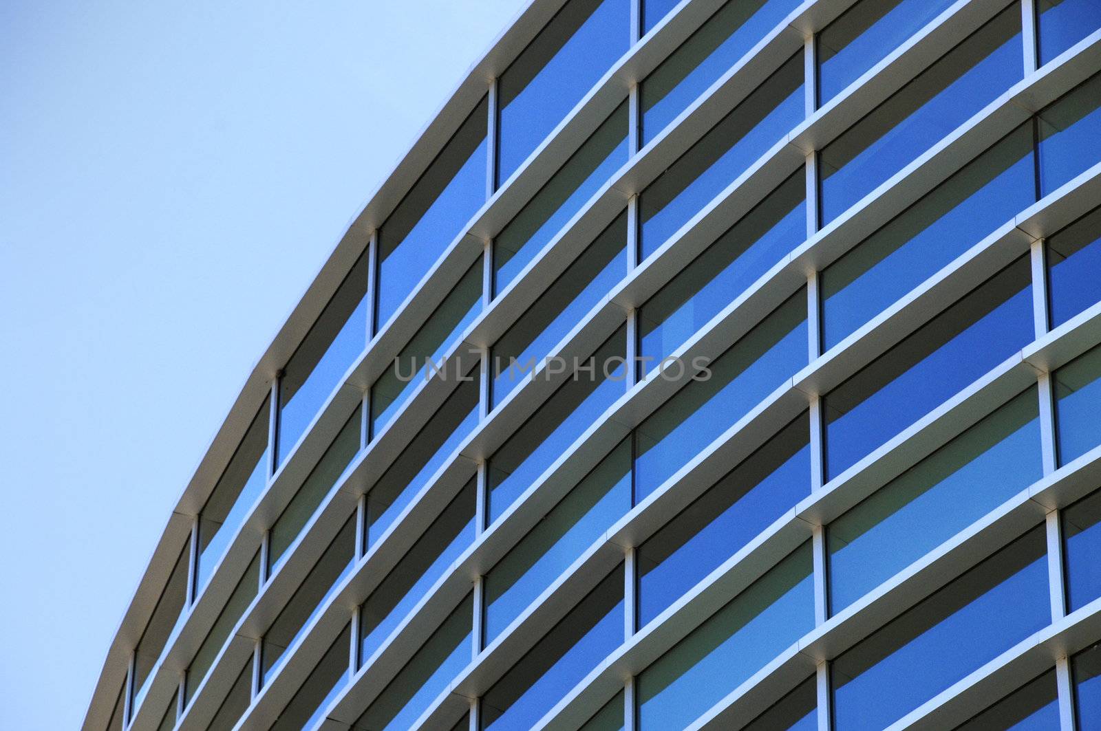 Curved exterior windows of a commercial office building reflecting a blue sky