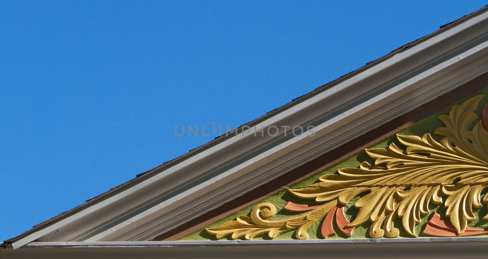 Portion of Gold, salmon, green carved woodwork on a victorian house with blue sky background