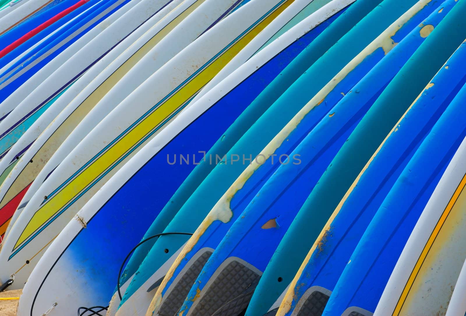A row of brightly colored rental surf boards with dings and dents from frequent use