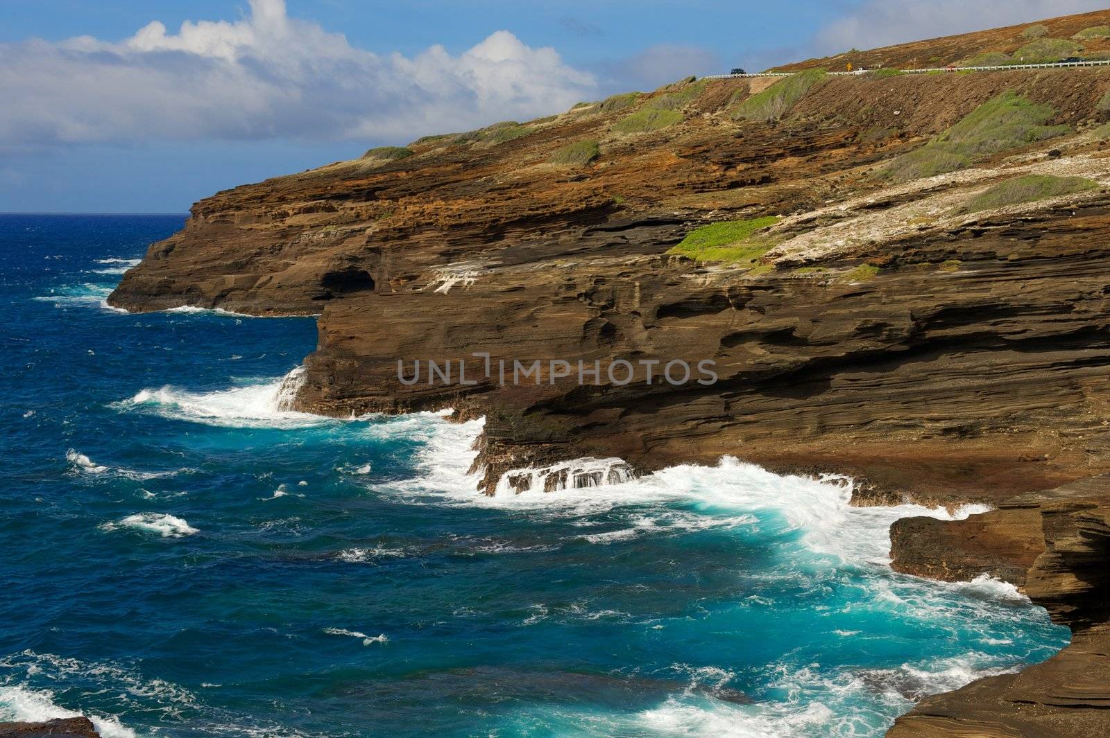 Oahu Cliffs with grass and beautiful, bright, blue, foamy waves and blue sky with clouds
