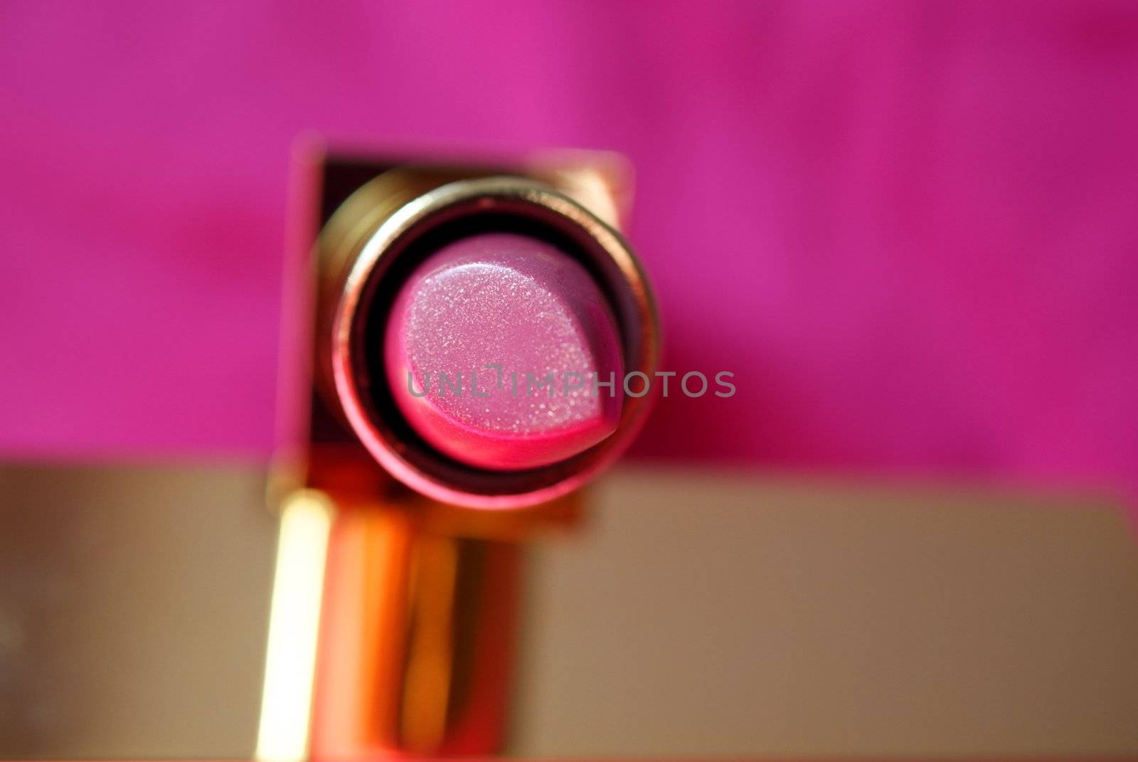 Pink lipstick in a gold tube on a pink and gold background. Shallow depth of field.