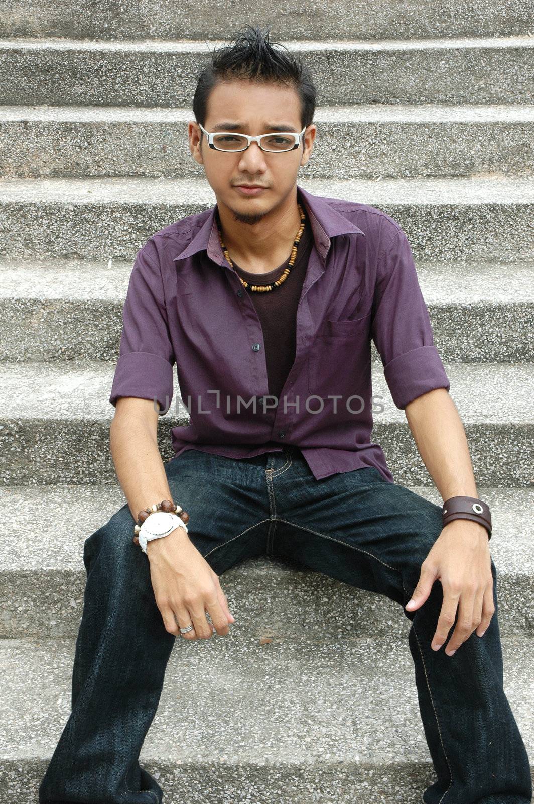 Handsome young Asian male with spectacles sitting on stairs