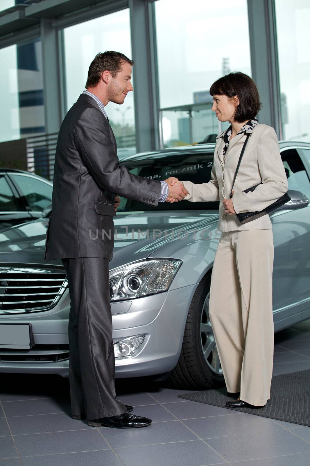 Car salesperson shaking hands with customer at showroom
