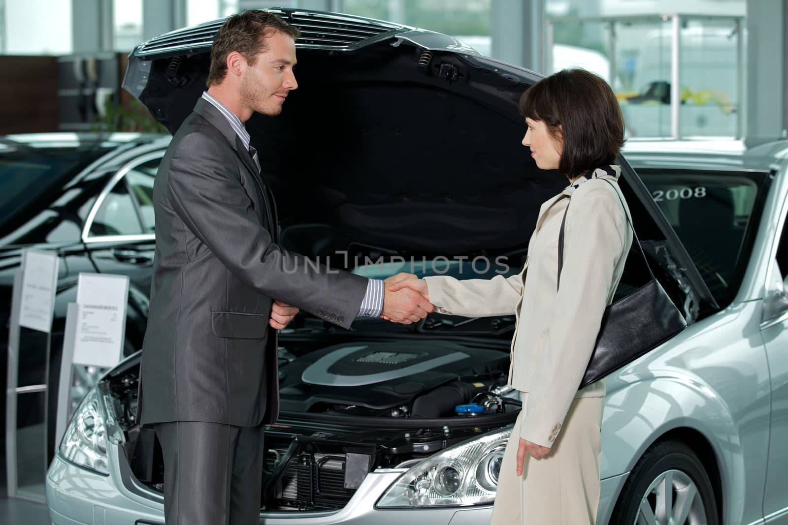 Car salesperson shaking hands with customer at showroom
