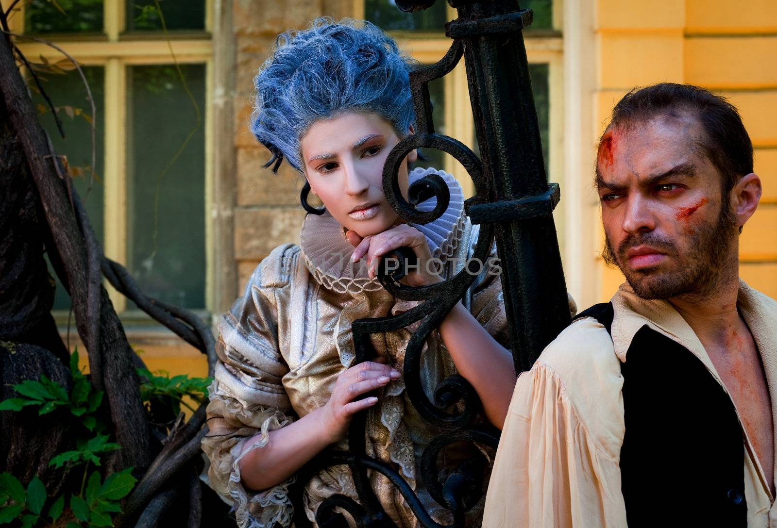 vampire and beauty in medieval costumes posing next to iron fence