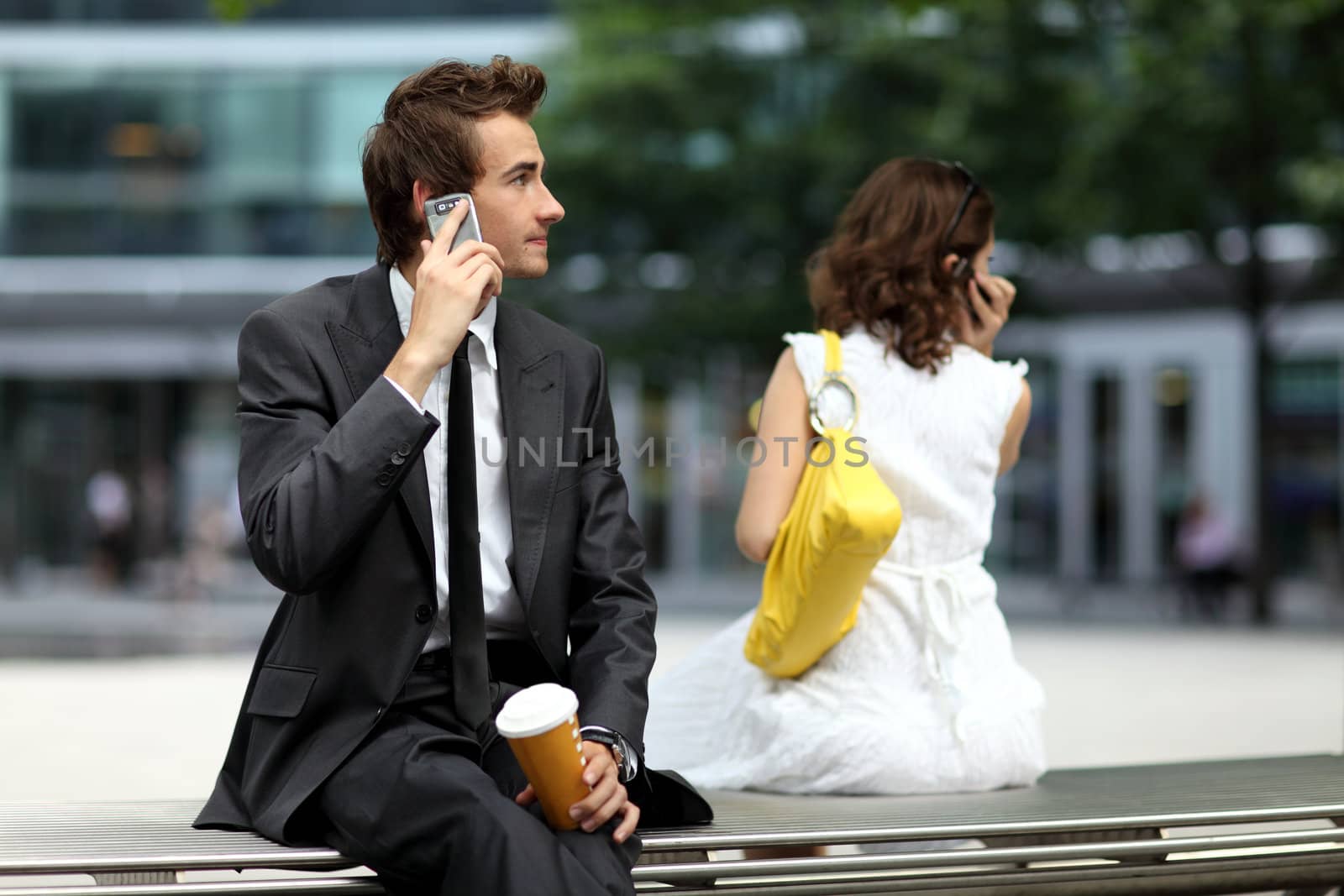 young caucasian businessman sitting on bench using his phone