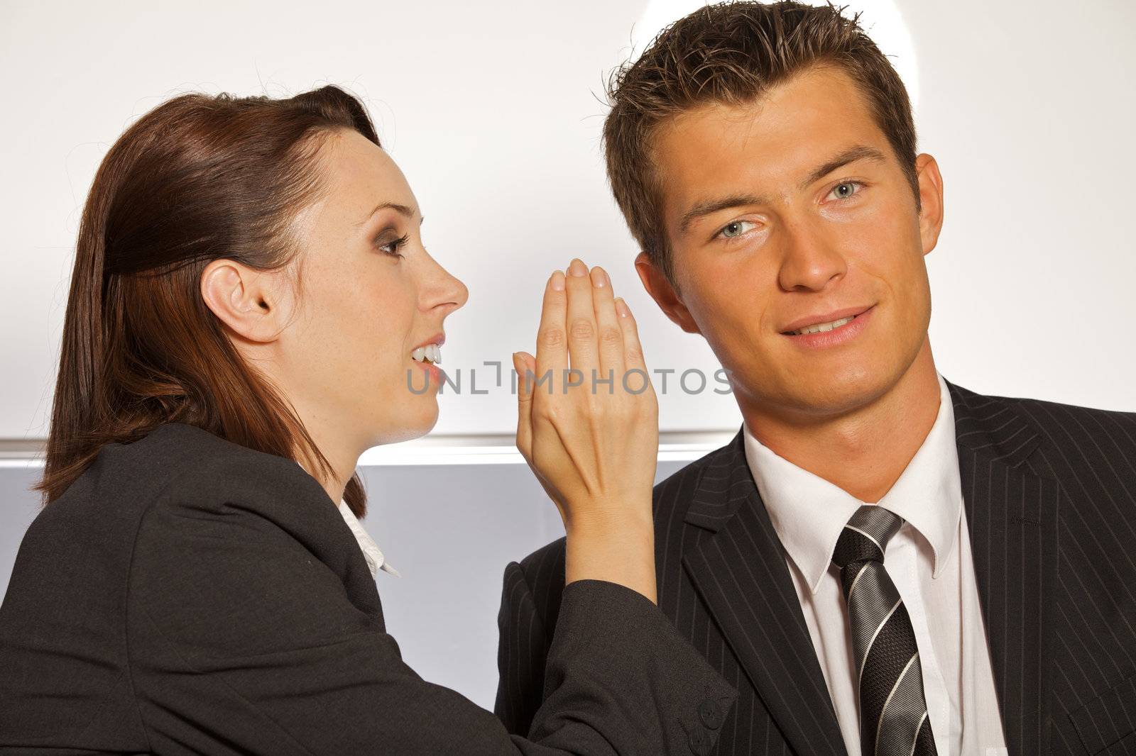 Businesswoman whispering in businessman's ear at office