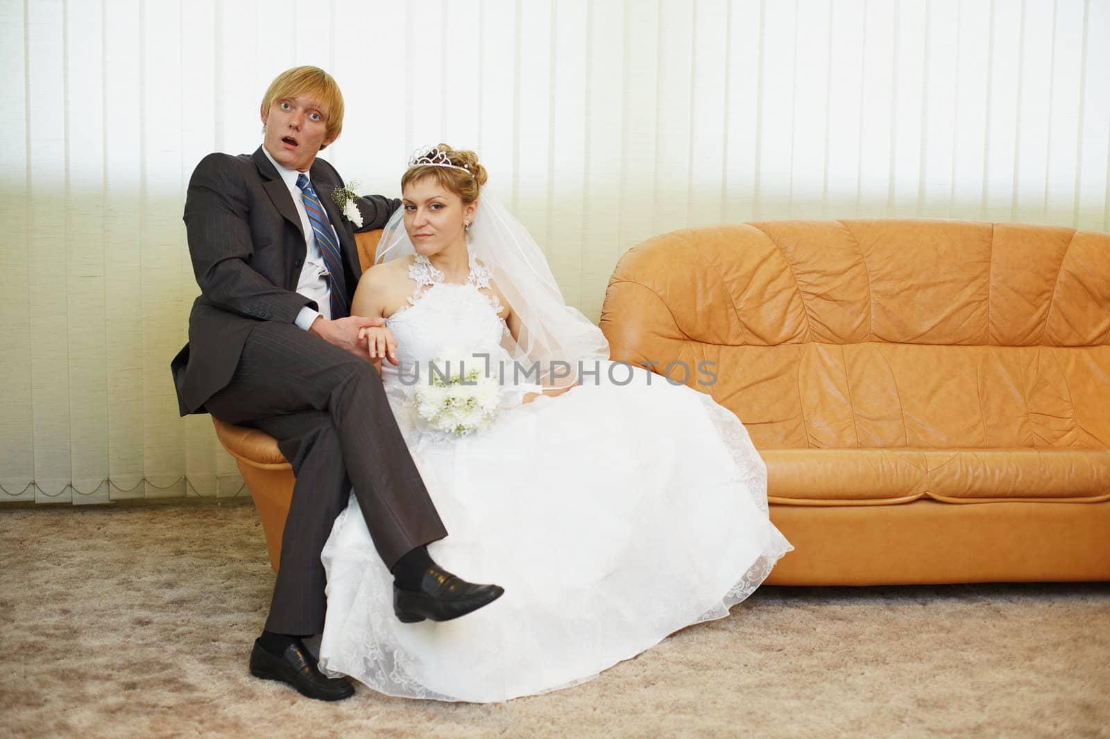 Amusing groom and the bride pose sitting on an armchair