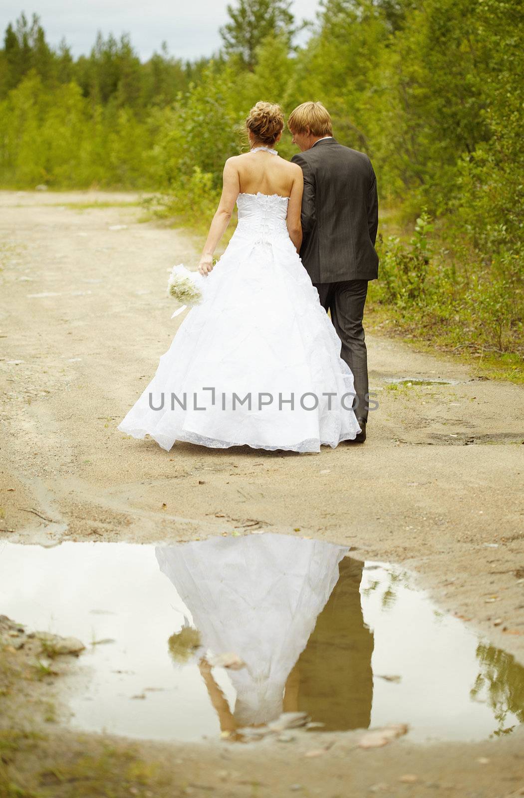 Newly-married couple walks on rural road after a rain