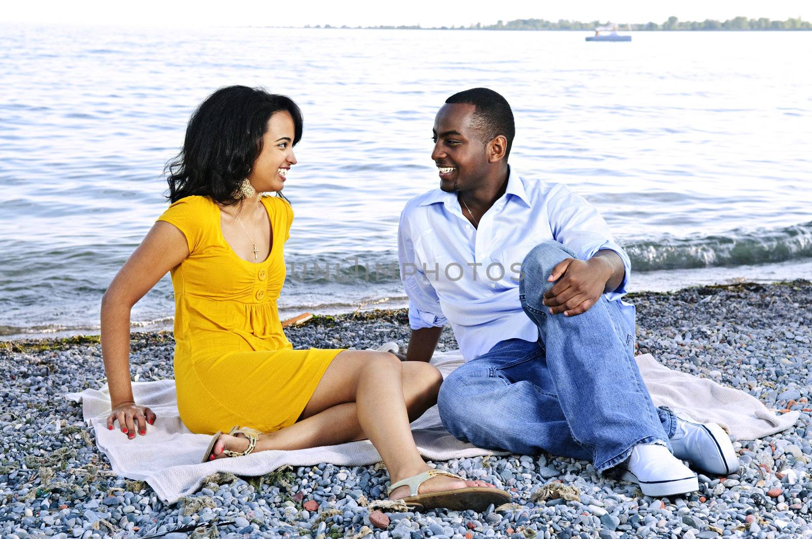 Young romantic couple looking at each other sitting on beach
