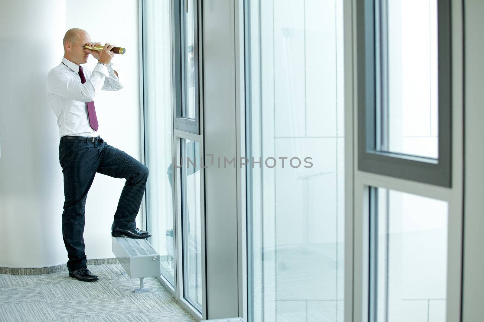 caucasian businessman spying using telescope thru office window