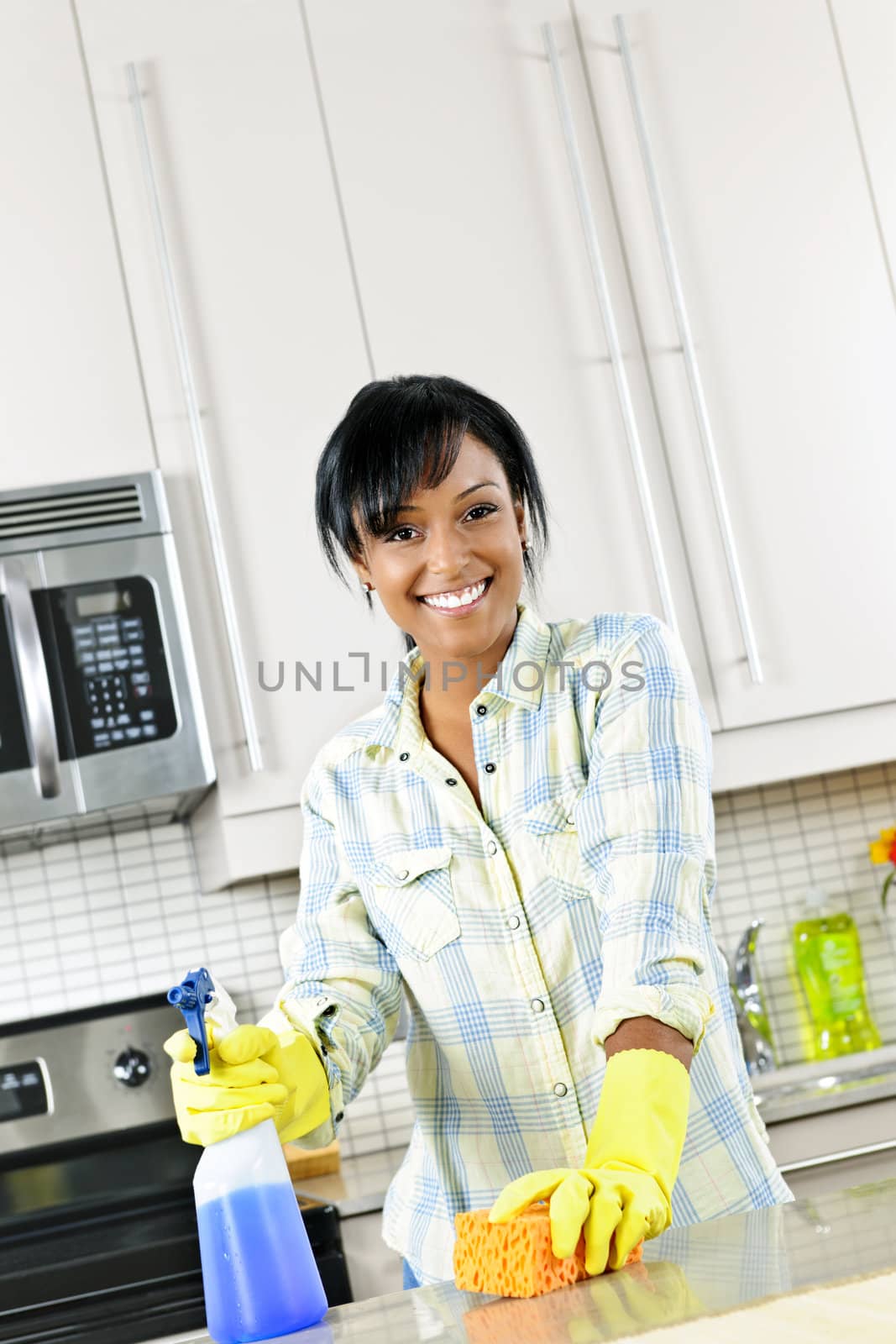 Smiling young black woman with sponge and rubber gloves cleaning kitchen