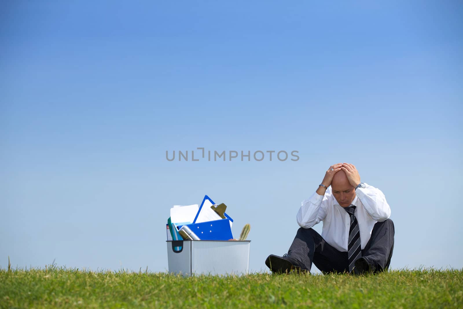 Cheerless businessman sitting next to basket full of files in park
