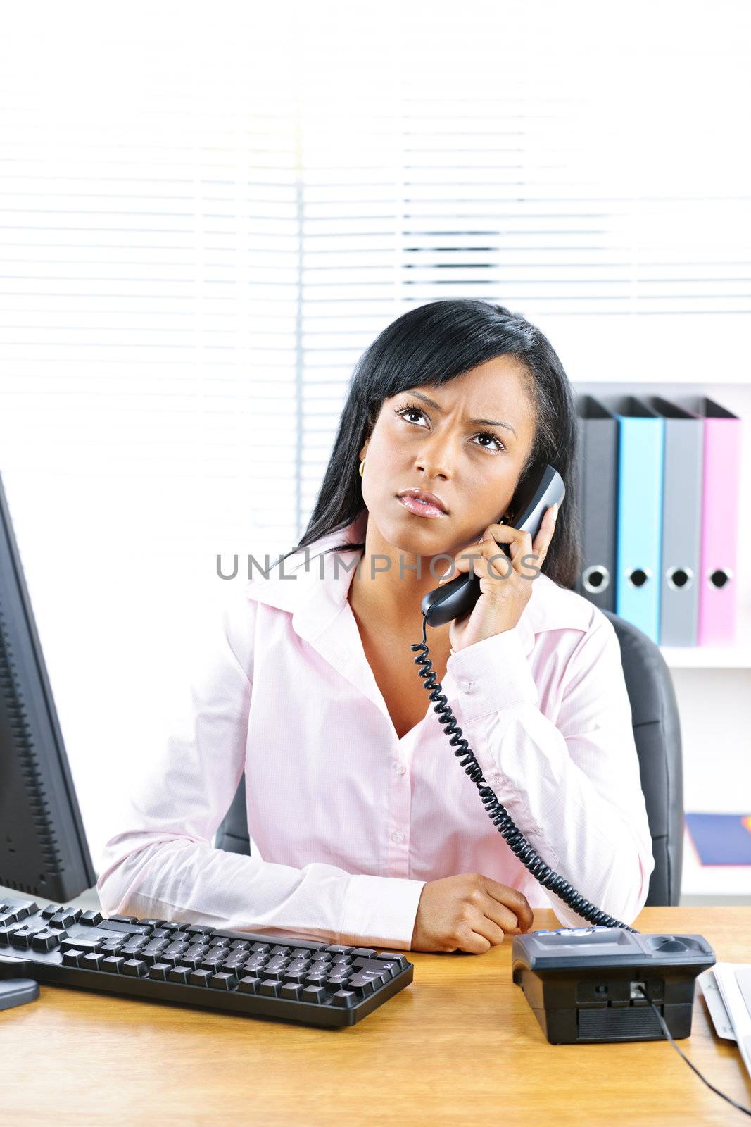 Concerned young black business woman on phone at desk in office
