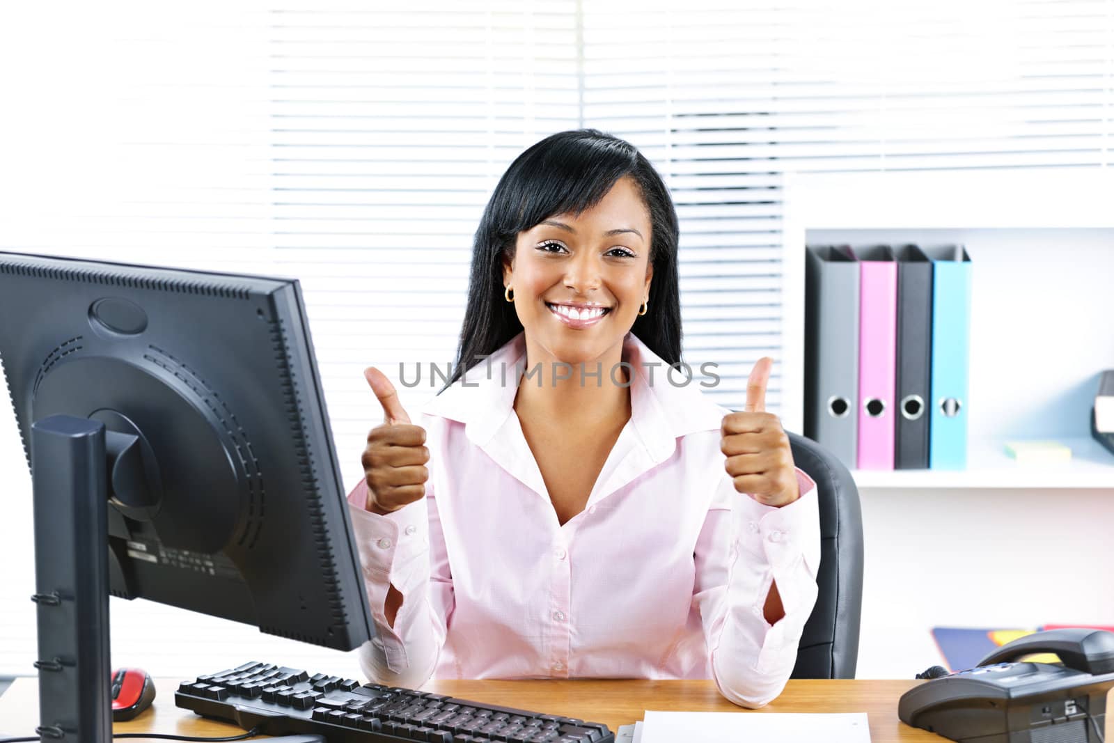 Smiling black business woman giving thumbs up gesture at desk in office
