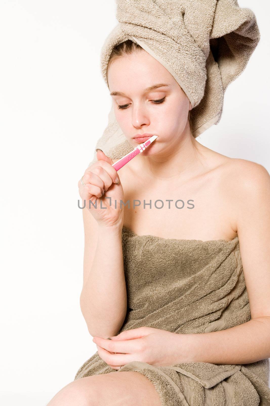 Young woman in towel on a white background brushing her teeth