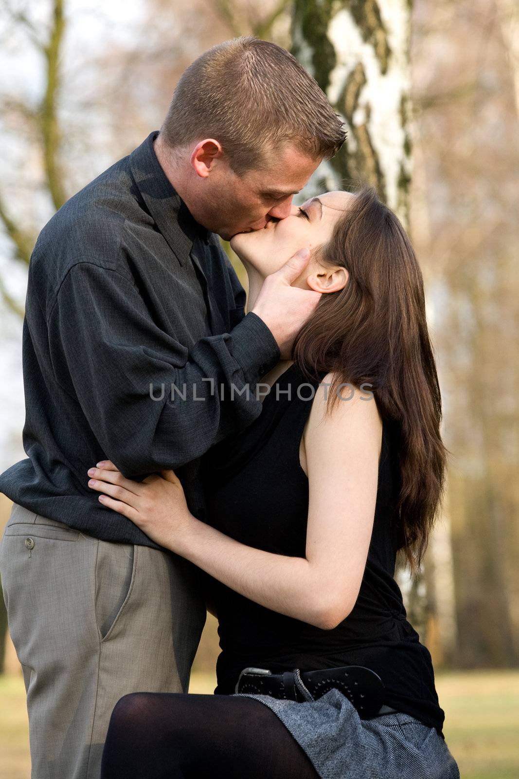 Man and girlfriend on a bench in a park kissing