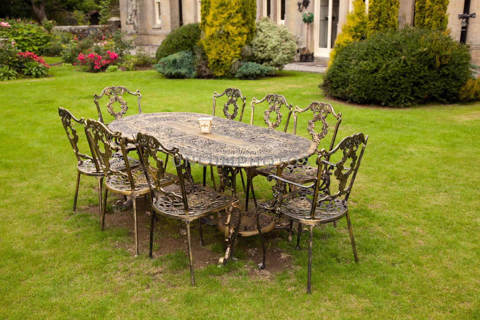 Old fashioned gold colored cast iron table and eight chairs on formal lawn