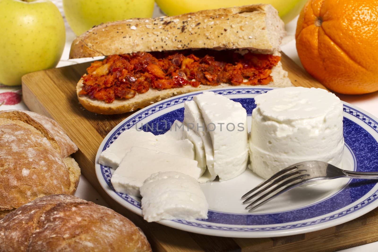 View of a dish of fresh cheese with sandwich of chorizo and fruit.