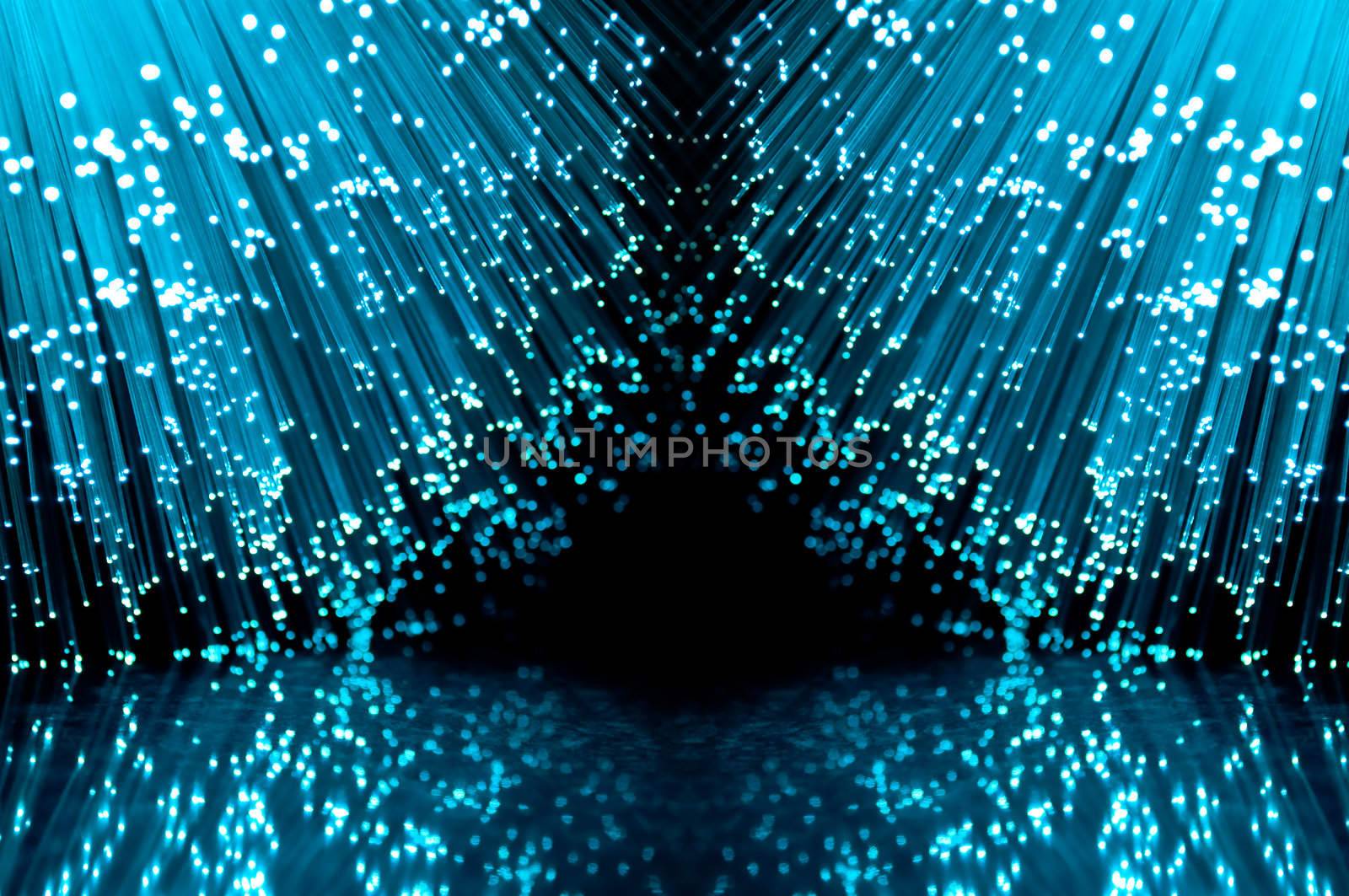 Two groups of blue illuminated fiber optic light strands against a black background and reflecting into the foreground.