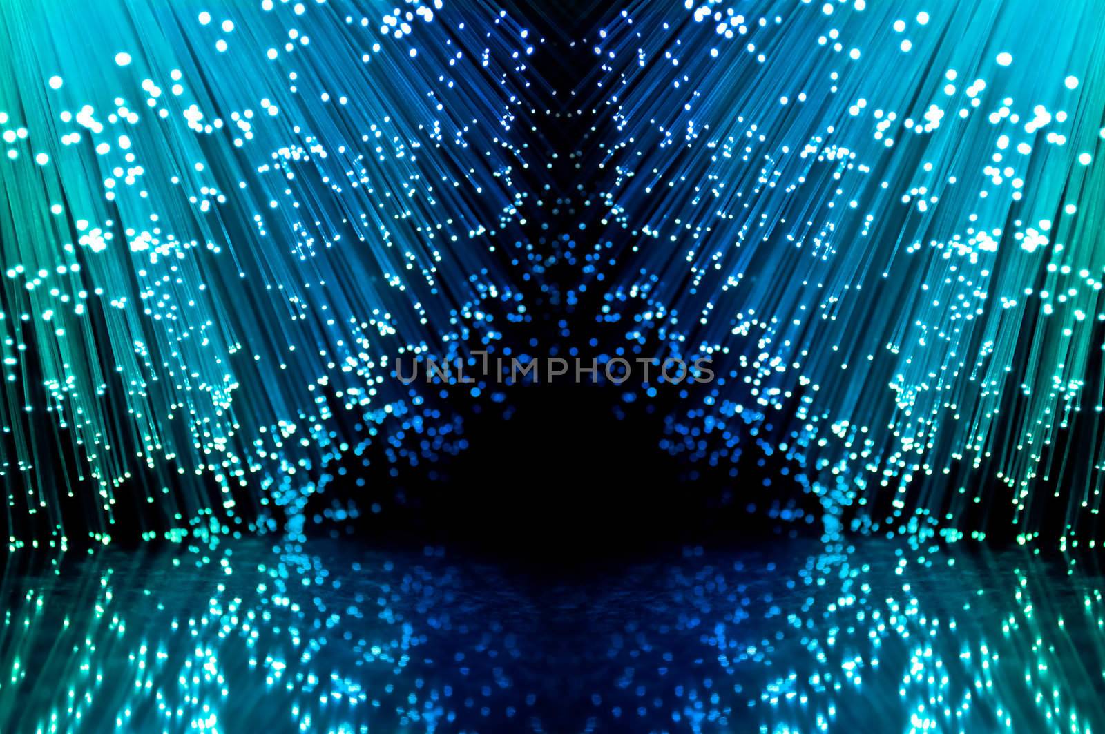 Close up on two groups of illuminated blue fiber optic light strands against a black background and reflecting into the foreground.