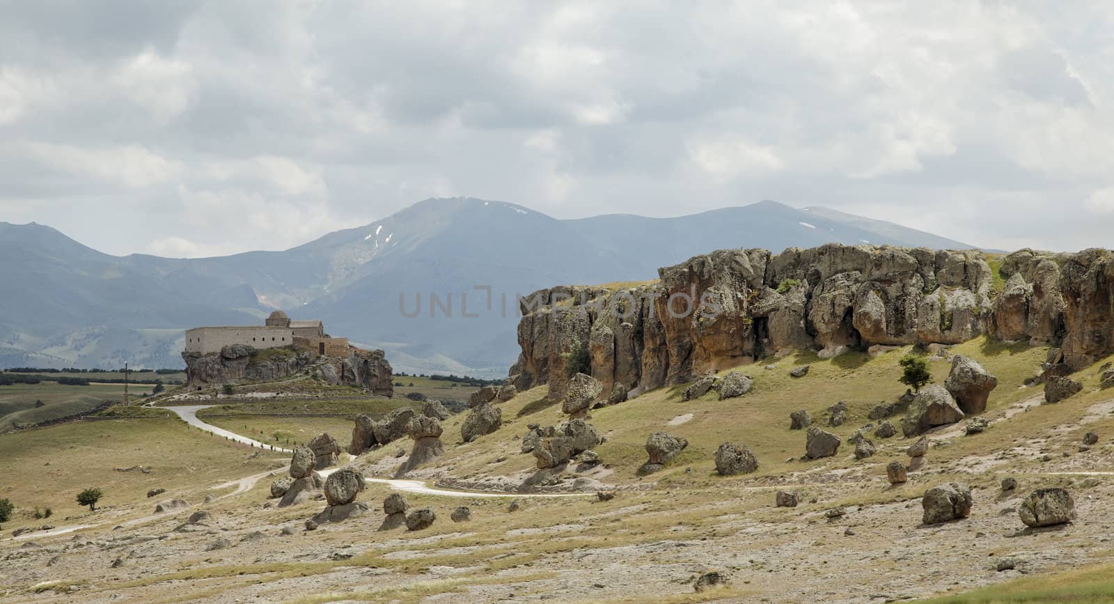 volcanic lava ash terrain with old church on a hill and mountain range in background Cappadocia , dirt tracks, cloudscape, landscape crop space and crop area