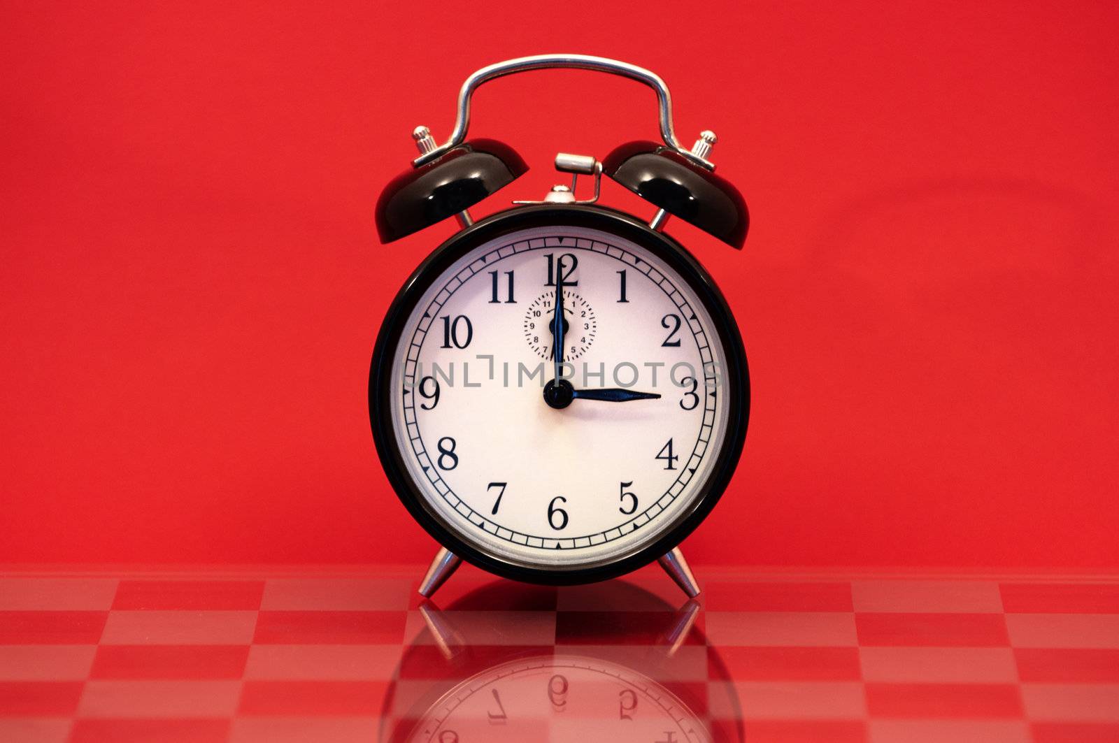 Vintage Alarm Clock Showing 3 O'Clock Isolated on a Red Background.