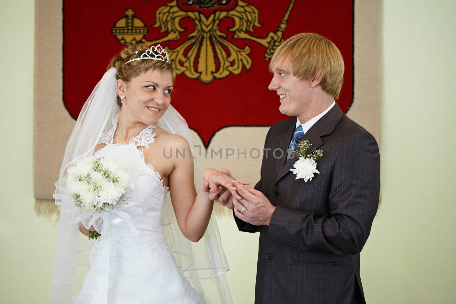 The bride and groom exchange rings on the background of the national coat of arms