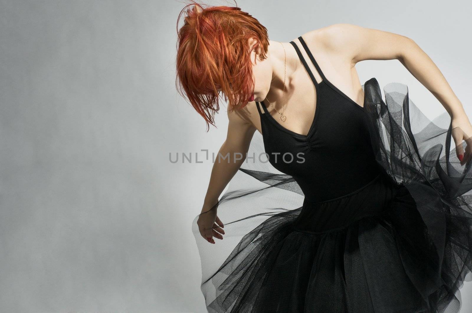 Beautiful ballerina wearing black tutu dancing over textured gray background