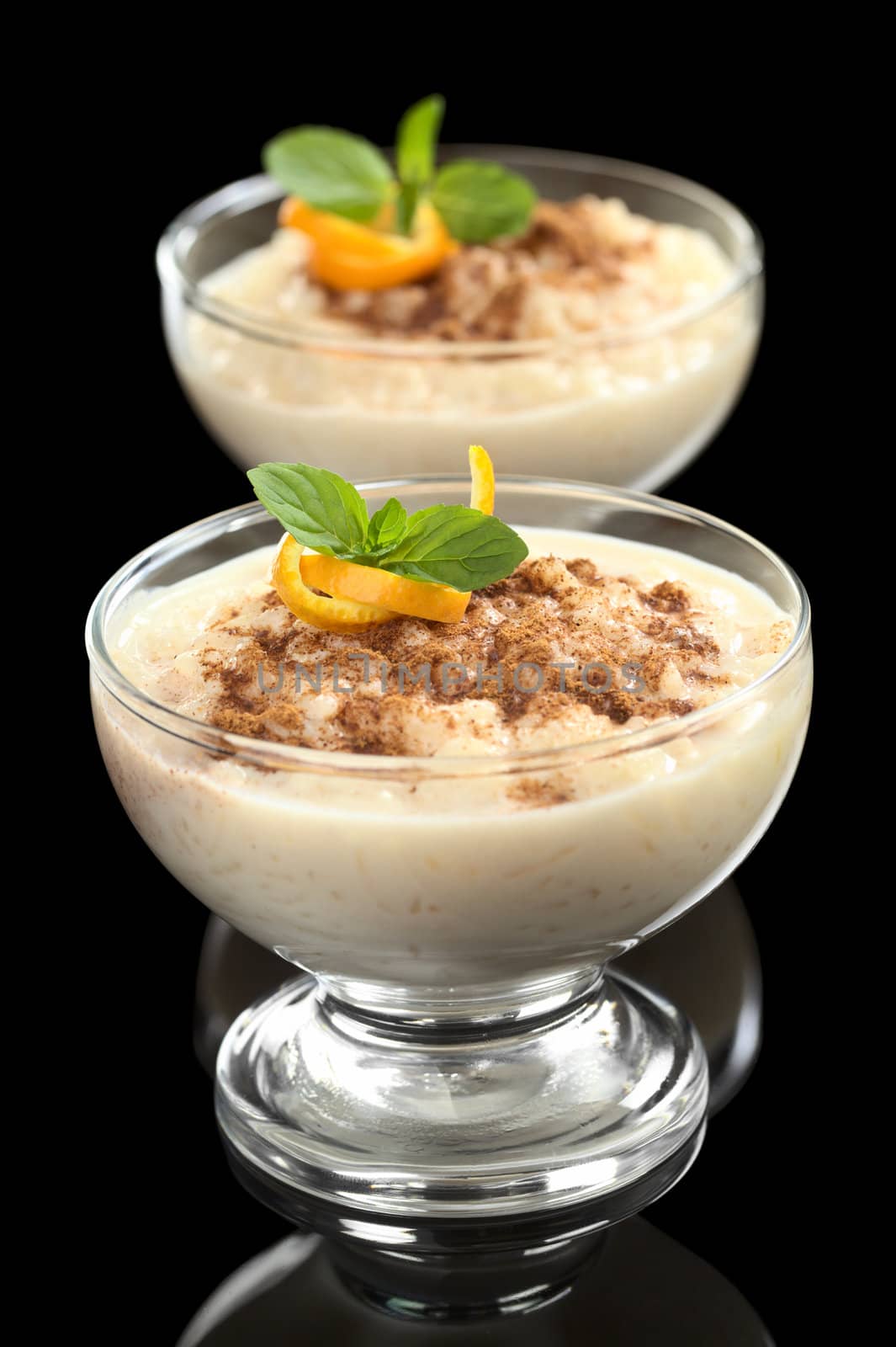 Delicious homemade rice pudding with cinnamon garnished with orange peel and mint leaf photographed on black (Selective Focus, Focus on the orange peel and the mint leaf on the first dessert)