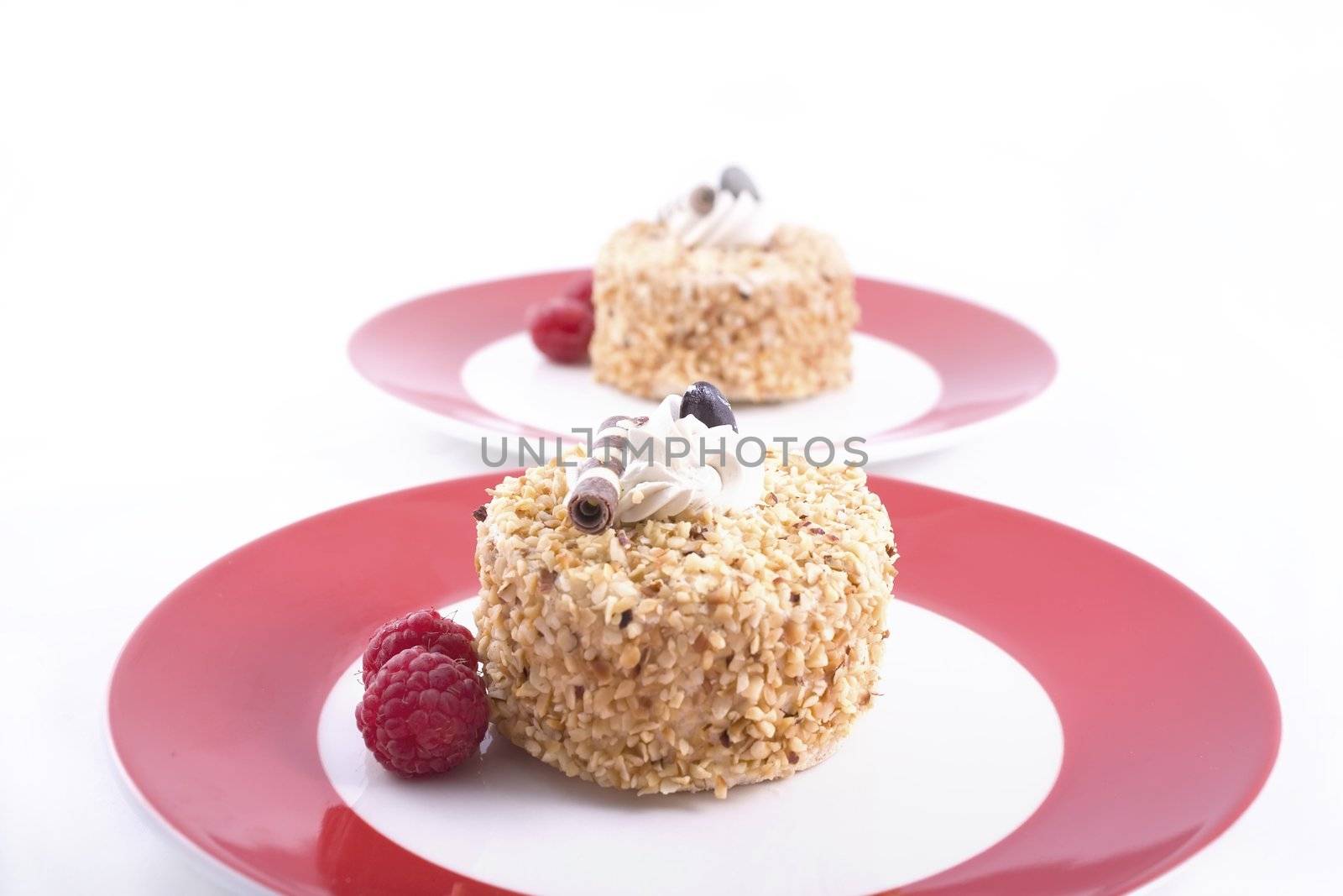 Two hazelnut cakes on red plates garnished with raspberries.  Isolated on white.