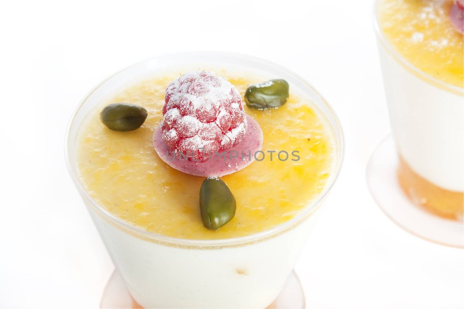 Close up of vanilla mousse topped with a sweet mango sauce, pistachios and a raspberry.  