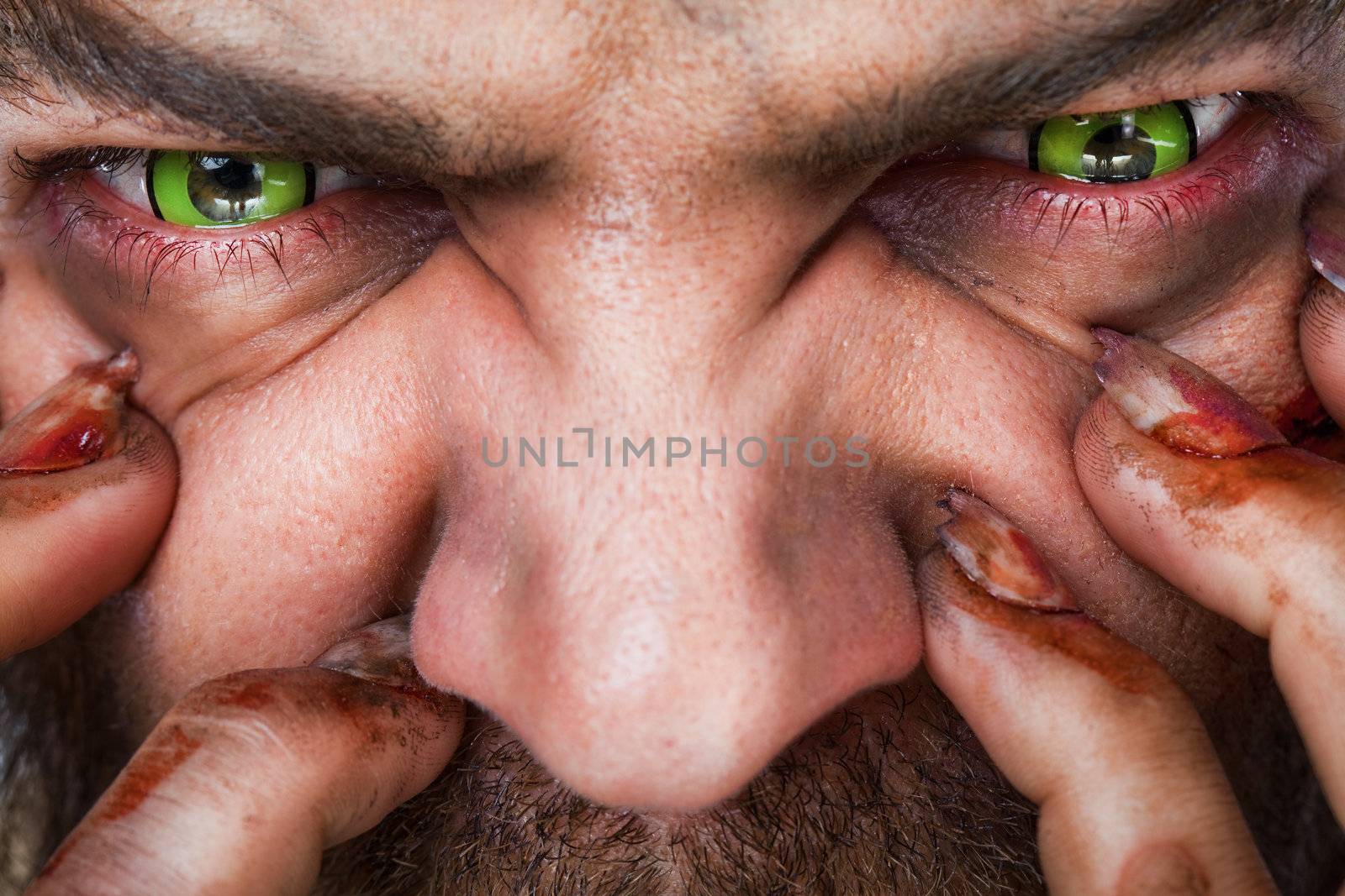 Cropped image of scary man's face with green artificial eyes and bleeding fingers